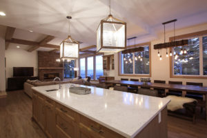 modern open concept kitchen with large lantern chandeliers lighting up a long island with a sink in it and a 16-person dining table up at silver star mountain resort community