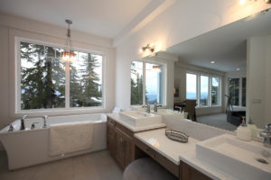 modern large bathroom with his and her white rectangular sinks, a stand alone with tub under large windows overlooking silver star resort in vernon, bc