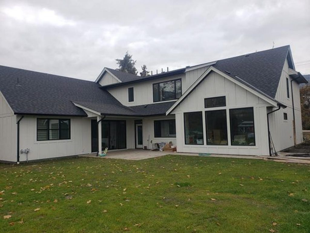 custom home build by parsons family homes with white wood paneling and dark wood outlining large windows set back at the end of a green lawn